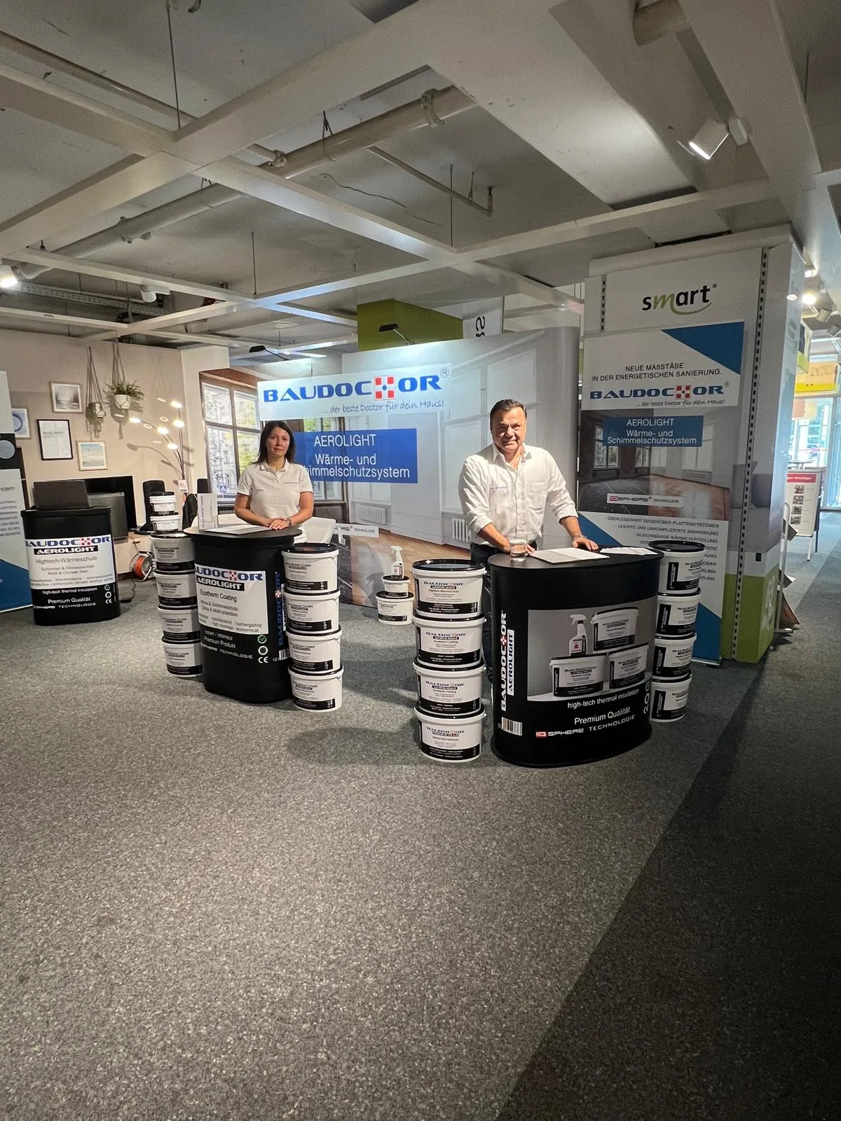 Metin Hidir hinter den AEROLIGHT Produkten am BAUDOCTOR Stand auf der Immobilienmesse Bad Segeberg 2026, mit Gebinden für Grundierung, Spachtel und Beschichtung.